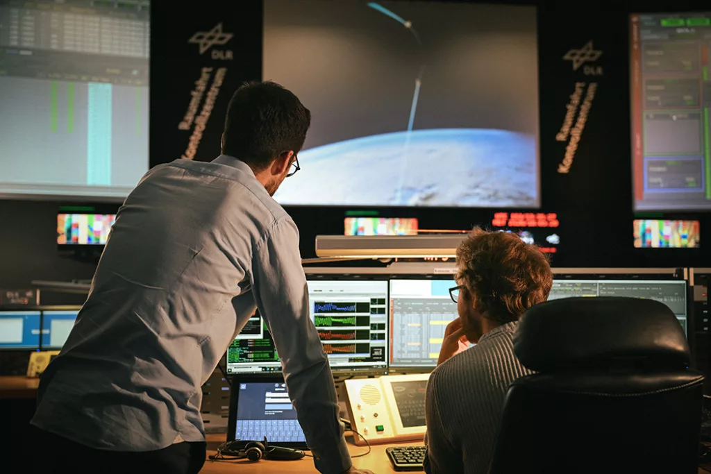 Two engineers in a control room looking a screens