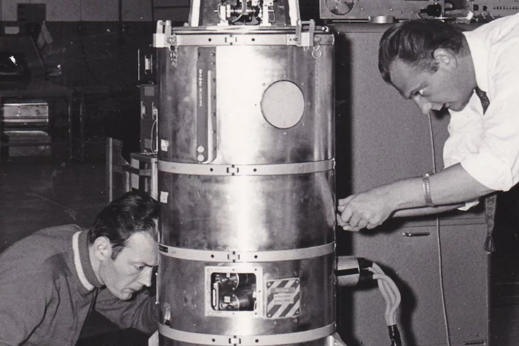 Two men working with a payload in a photo from the 1960's.