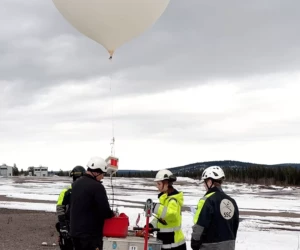 A captive balloon was used to lift the CanSats to 150 m altitude before dropping them towards the ground. White ballon towards the sky, with persons in the front of the picture.